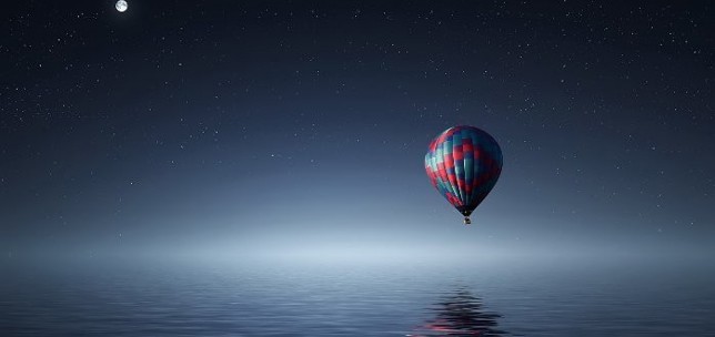 Hot air balloon over the ocean at night with a starry, clear sky