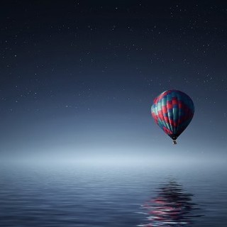 Hot air balloon over the ocean at night with a starry, clear sky