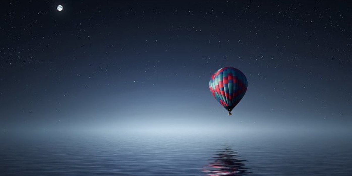 Hot air balloon over the ocean at night with a starry, clear sky