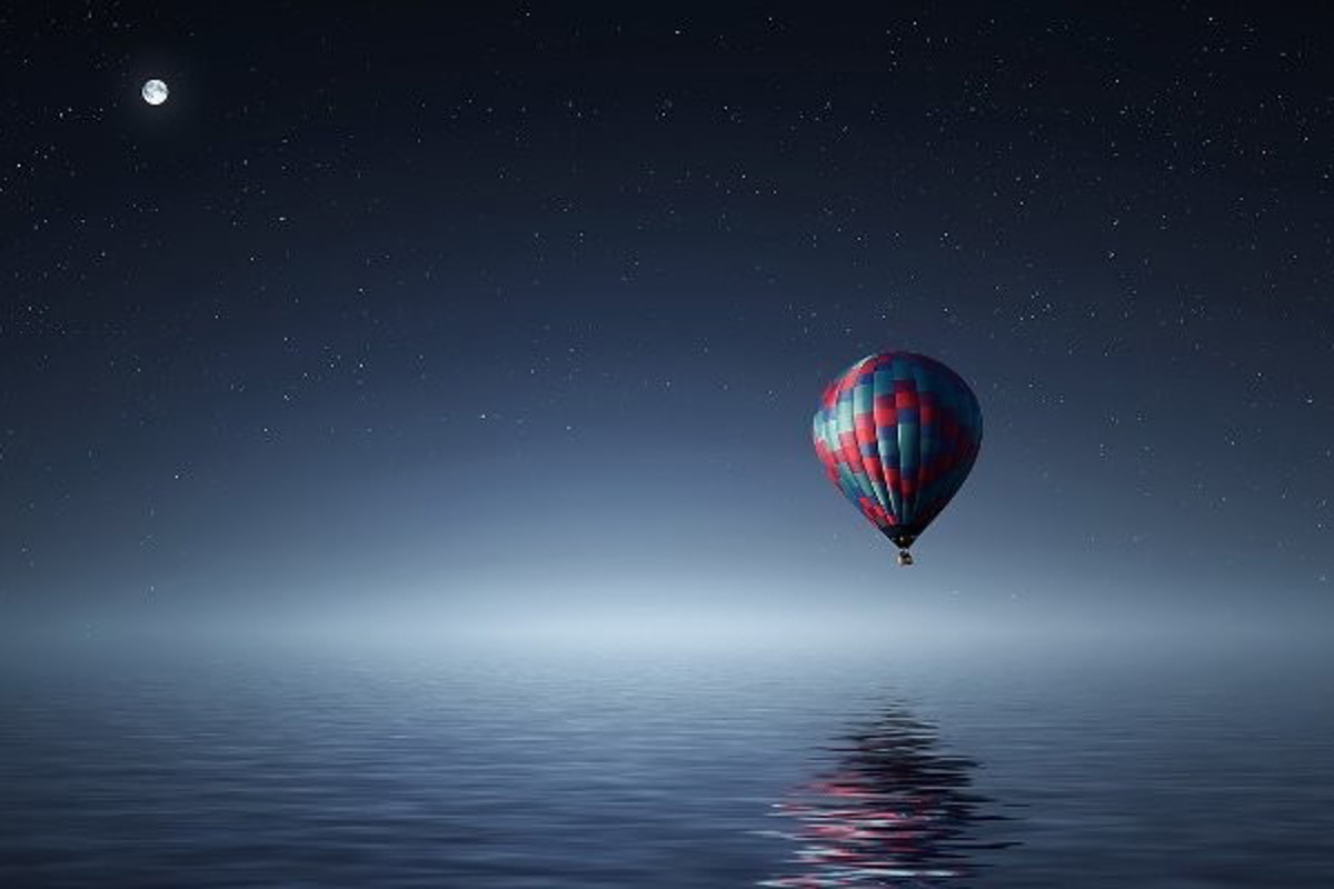 Hot air balloon over the ocean at night with a starry, clear sky